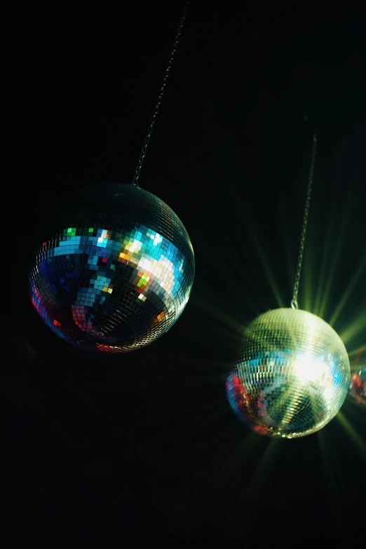 two disco balls hanging from strings are glowing