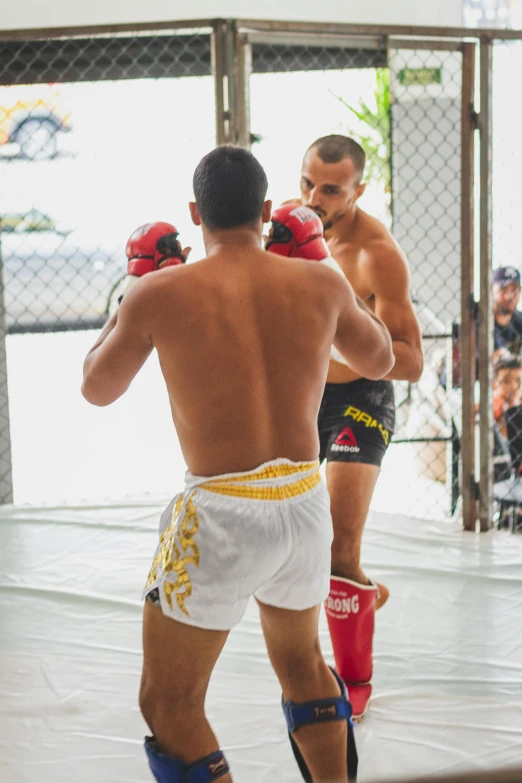 two boxers, one wearing white shorts and one with red boxing gloves, are in the middle of a practice area