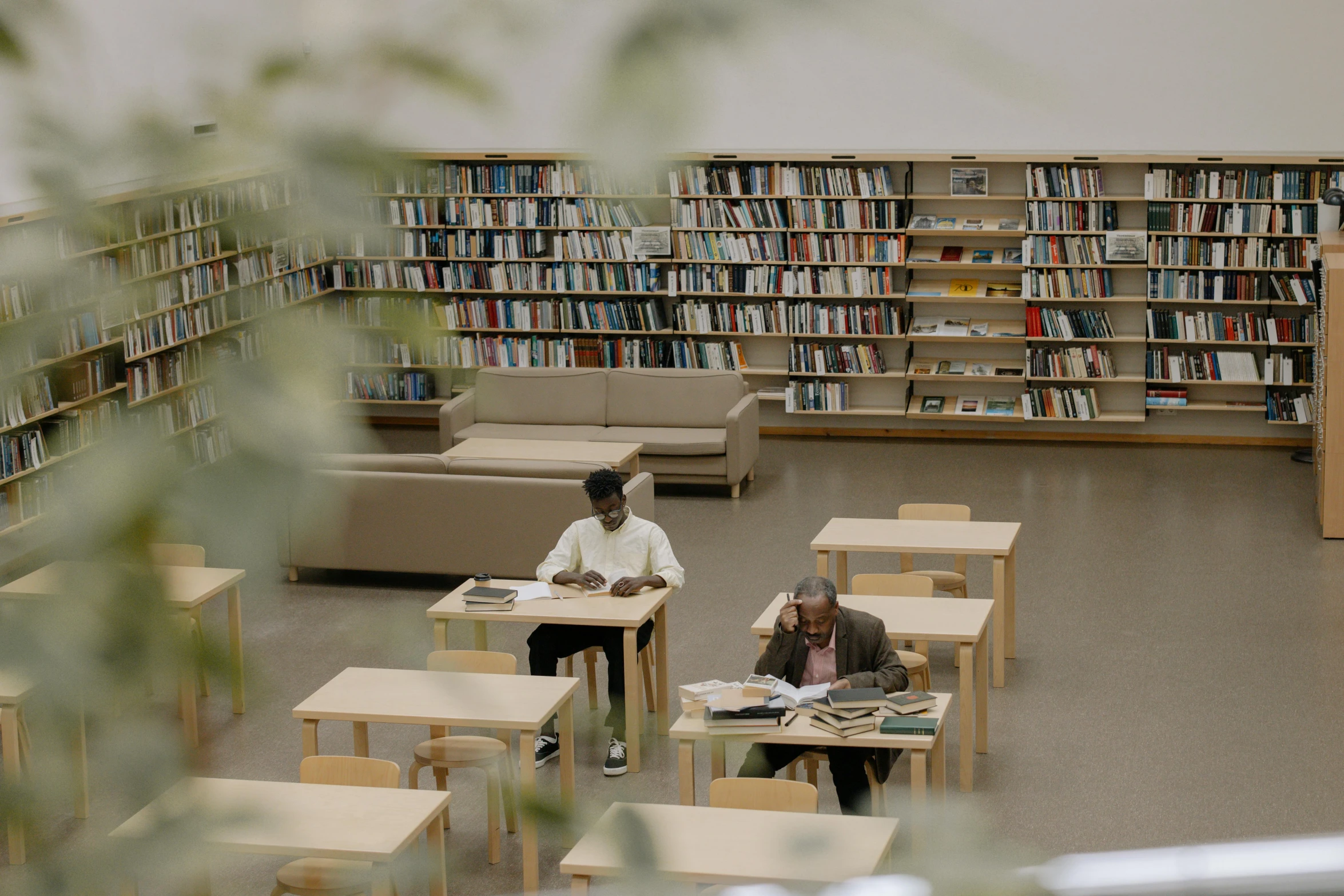 two men sit at tables in front of shelves filled with books