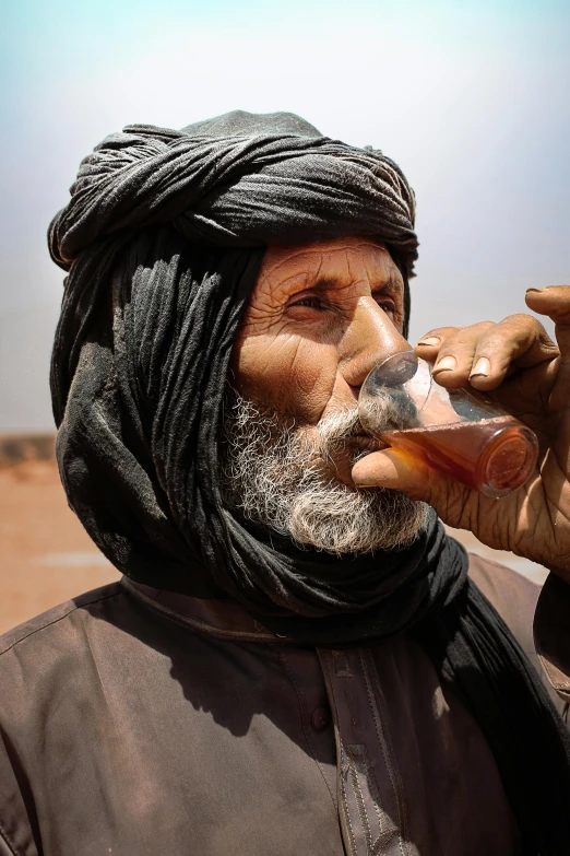 an older man with a scarf on drinking from a bottle