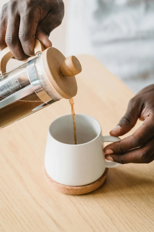 a man pouring coffee into a cup on top of a wooden table