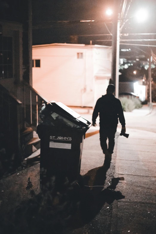 a man walking next to a garbage can in the dark