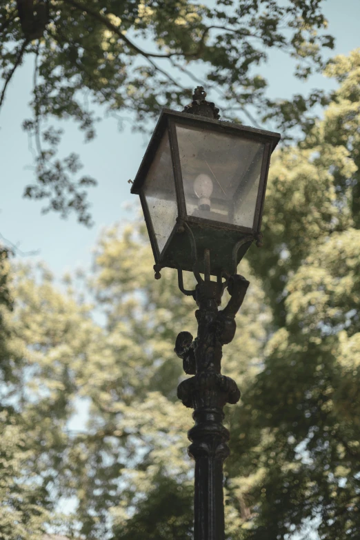 an old fashioned street lamp with some green trees