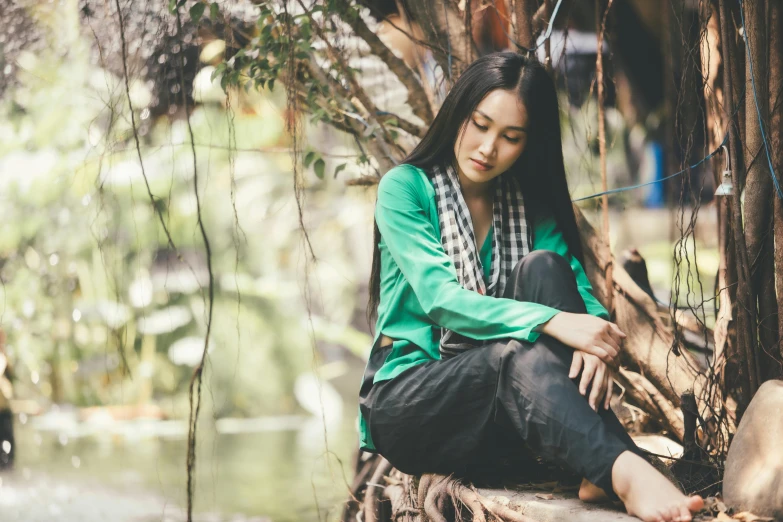 a girl sitting by a tree on a log in the woods