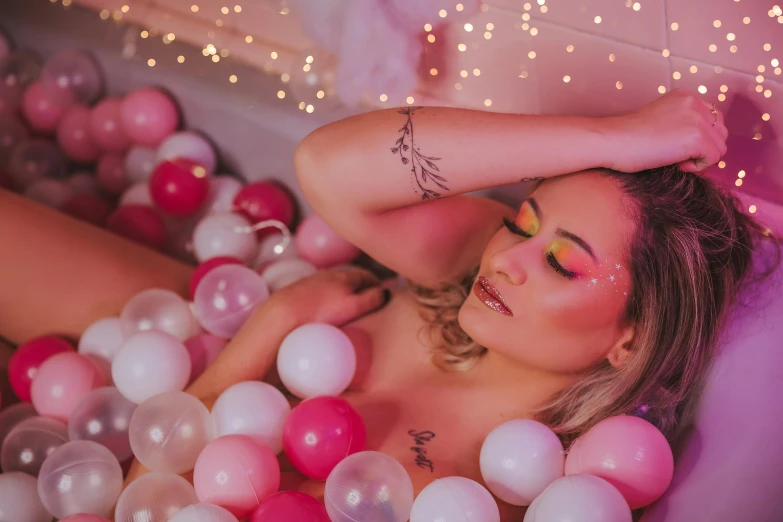 a girl laying in a bubble bath, surrounded by balloons