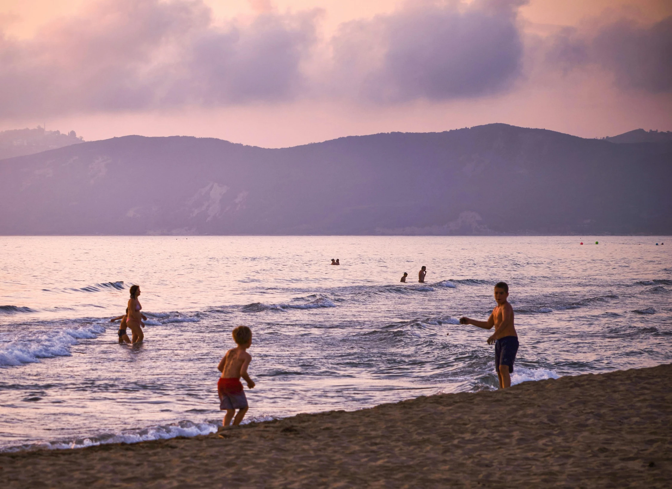 people walk along a beach with mountains in the distance