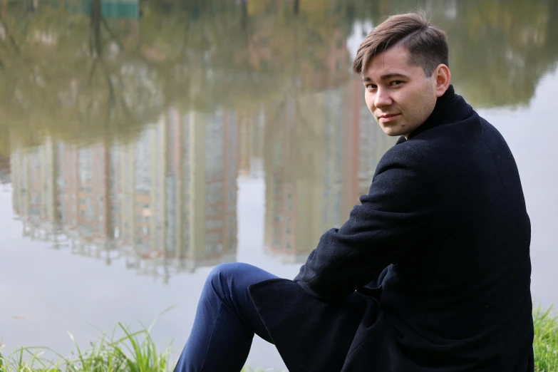 a man in a coat is sitting by a pond