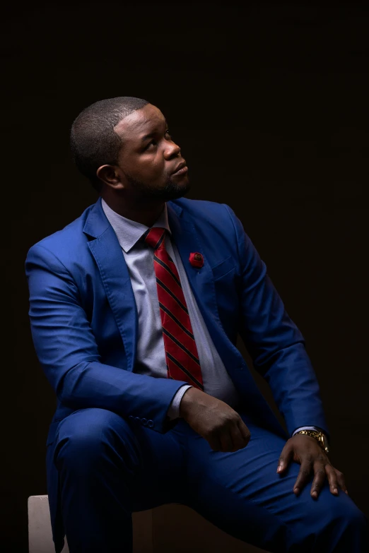 a man sitting in a chair wearing a blue suit and red tie