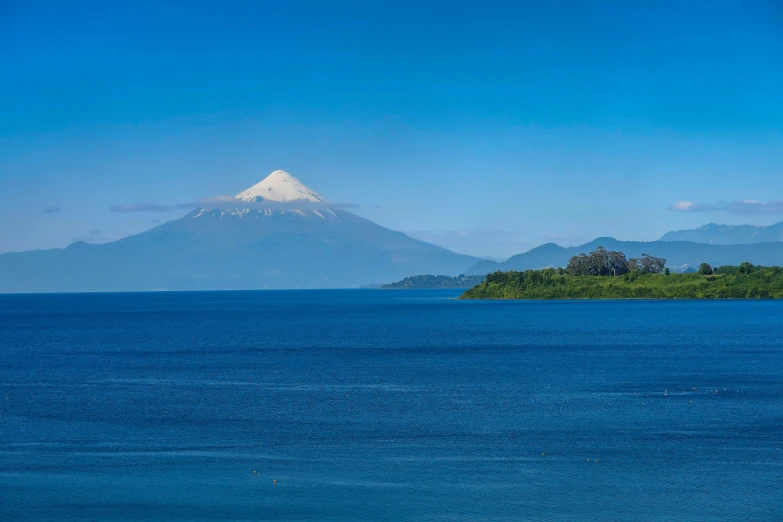 a island with trees near the water and snow capped mountains