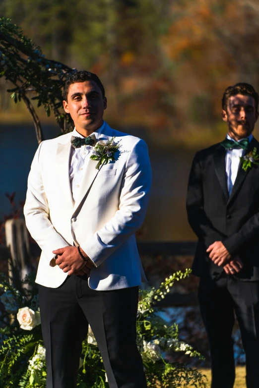 two grooms standing outside in tuxedos at the ceremony