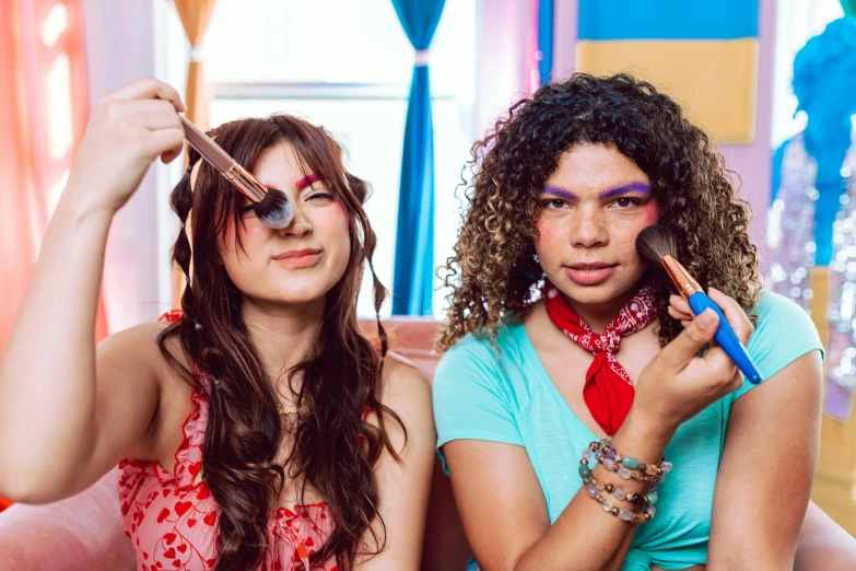 two pretty young ladies holding makeup brushes in their hands