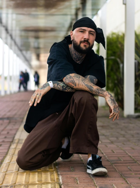 a man with tattoos sits and poses on the sidewalk