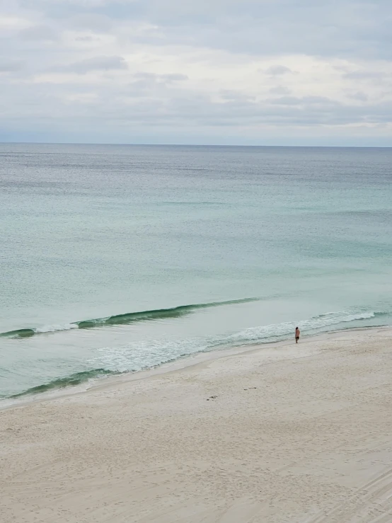 two people walking along a beach next to the ocean