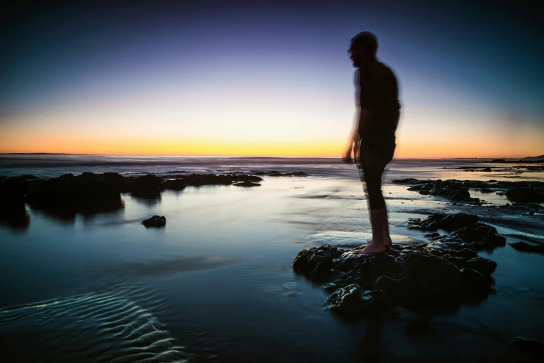 the silhouette of a man standing on top of rocks near water