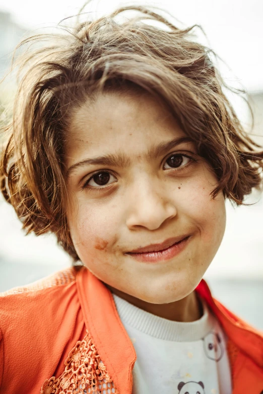 a small girl wearing an orange jacket and smiling