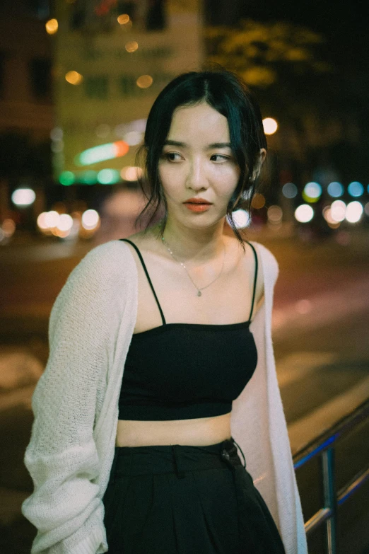 a woman standing on the side walk at night with a long sleeve top over her head