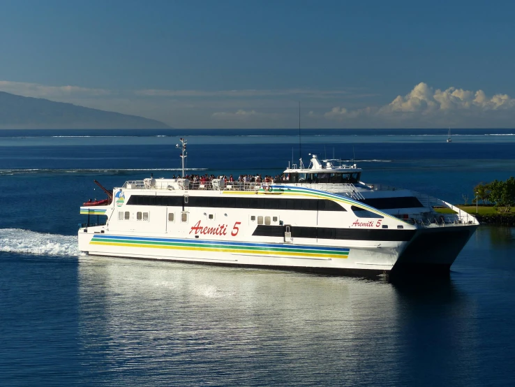 a large ferry sails on the blue water near land