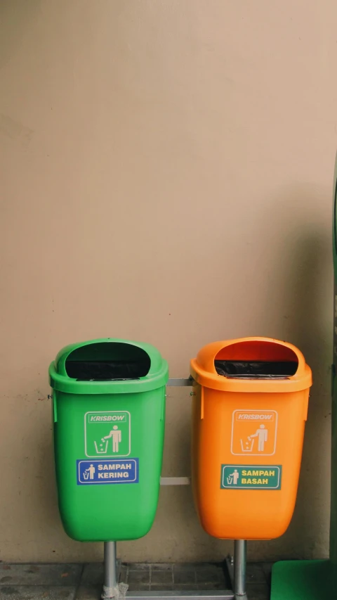 two different colors of trash cans against a tan wall