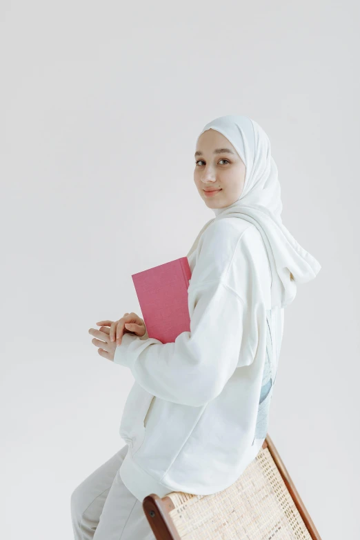 a woman in a hijab holds a binder and looks at the camera