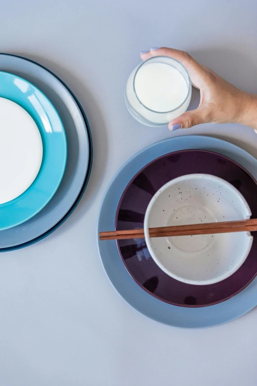 hand holding chopstick next to small bowl and plate on table
