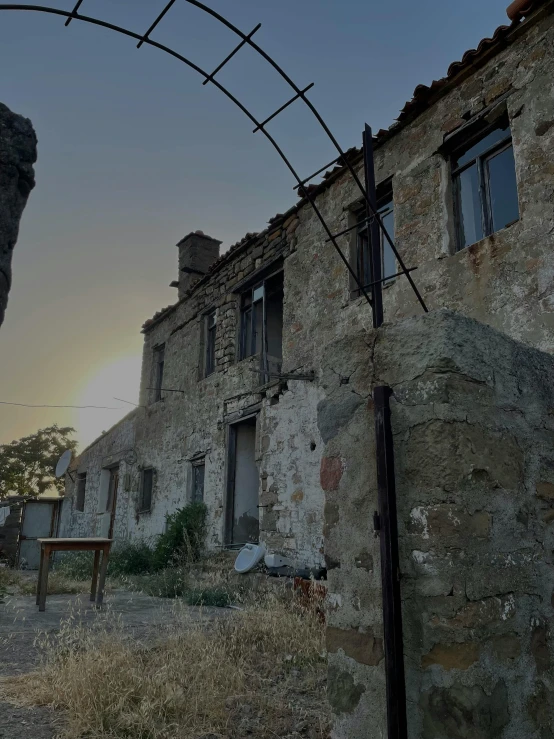 an old abandoned building near a field at sunset