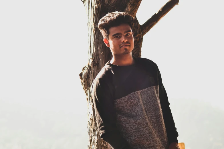 the young man poses in front of a tree