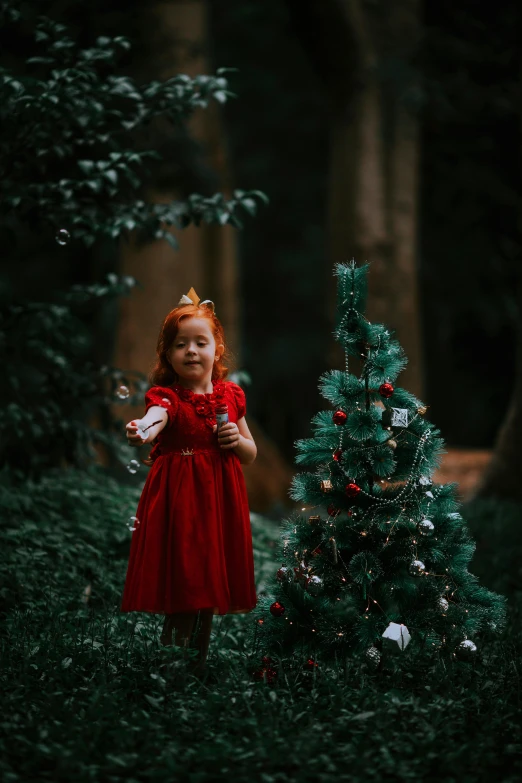 little red haired girl standing in front of a christmas tree