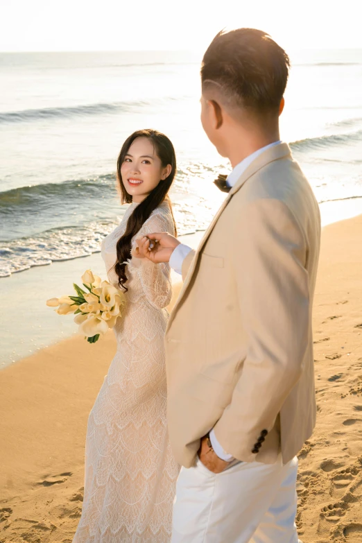 a beautiful asian bride and groom stand on the beach