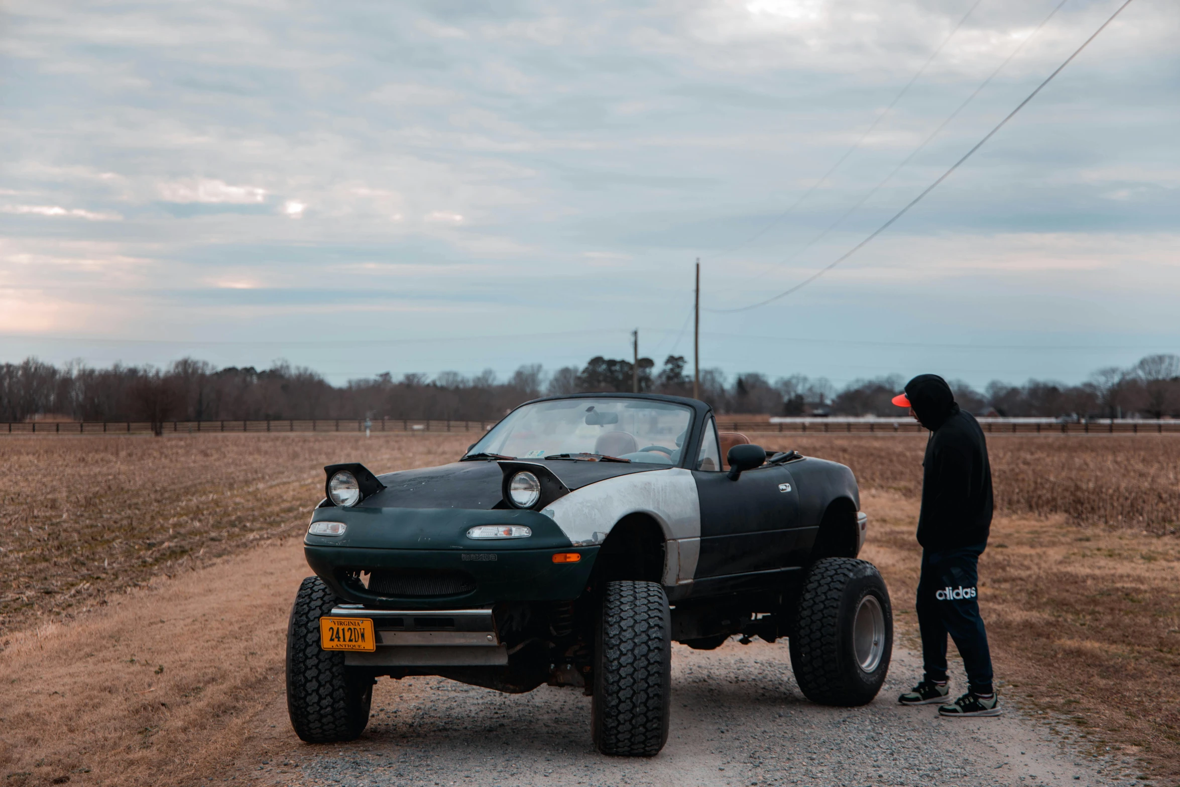 a man in black jacket standing by vehicle in field