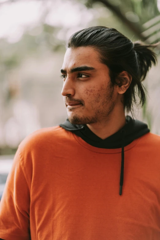 a man wearing an orange shirt with a ponytail in the side