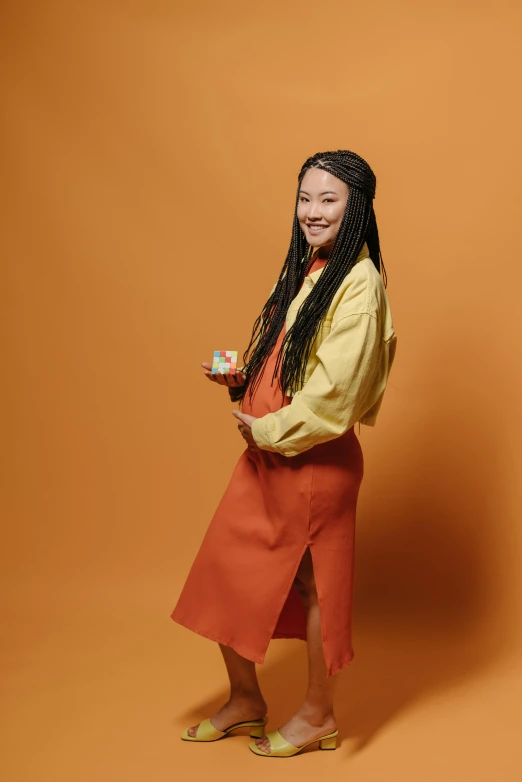 a woman poses in an orange skirt and coat with her hair in ids