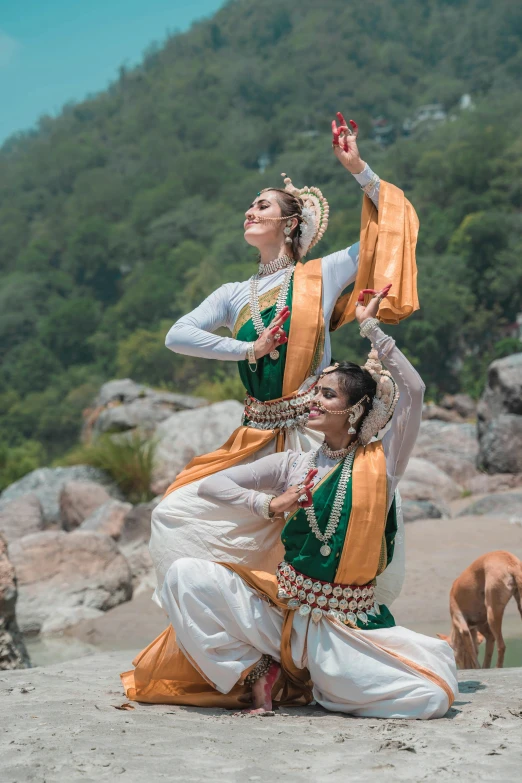 two women in indian clothing doing yoga on the beach