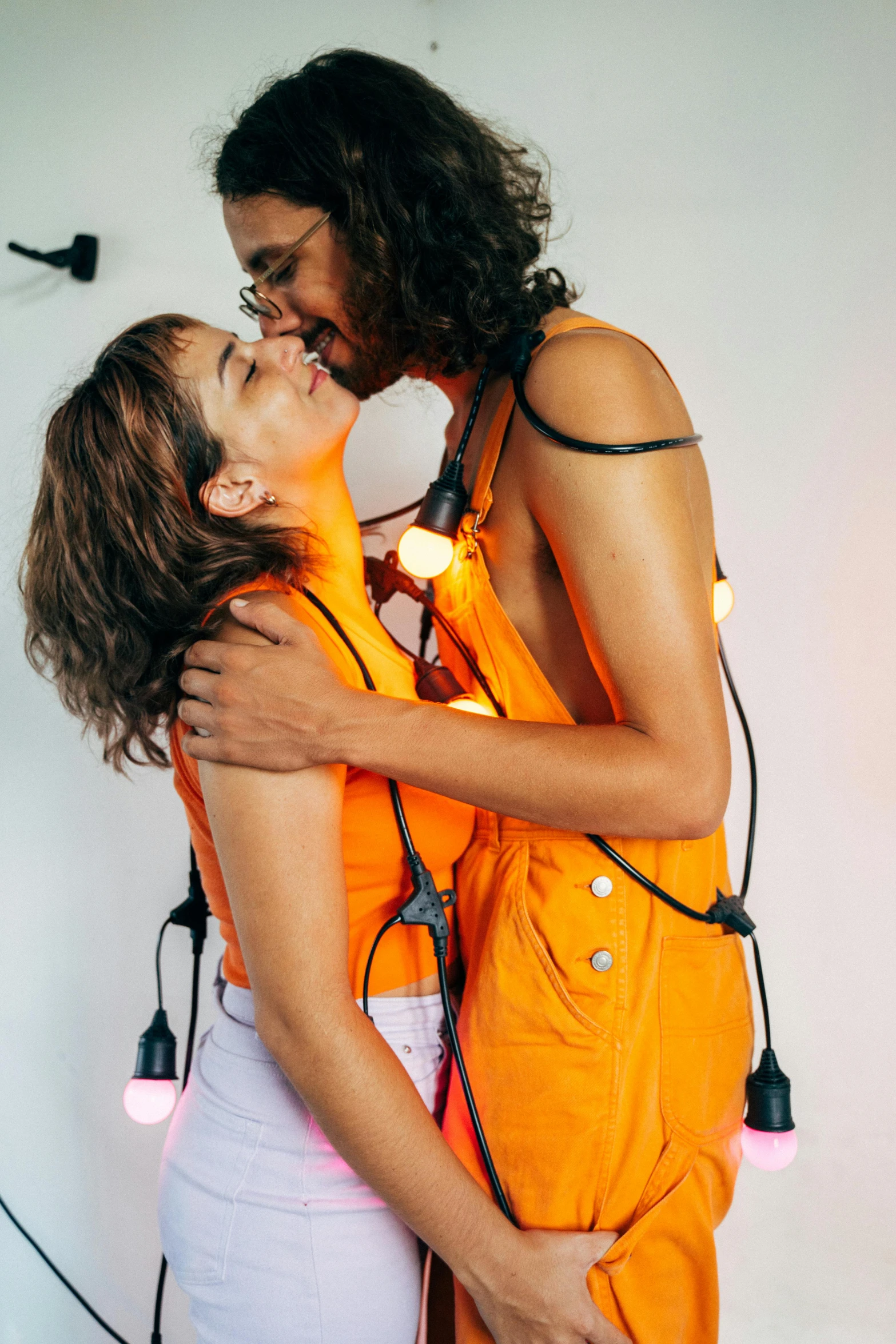 a man and woman kissing with a string of lights on the wall