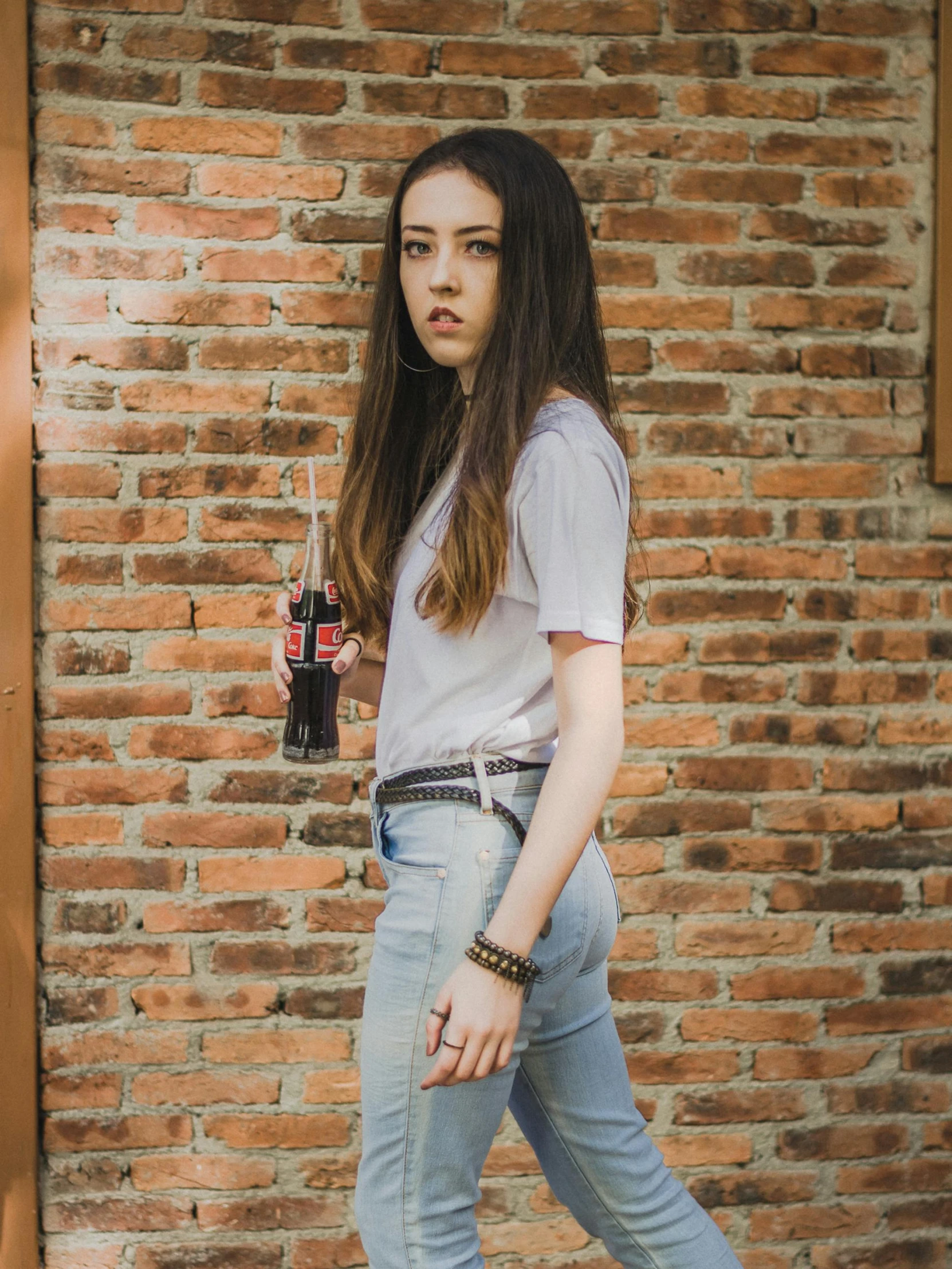 a woman walking by a brick wall and holding an iced beverage