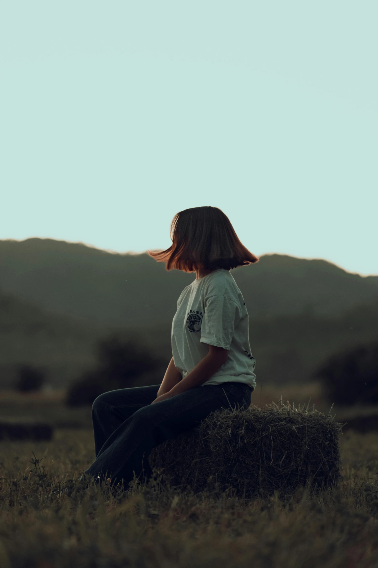 woman sitting on a hay bale looking off into the distance