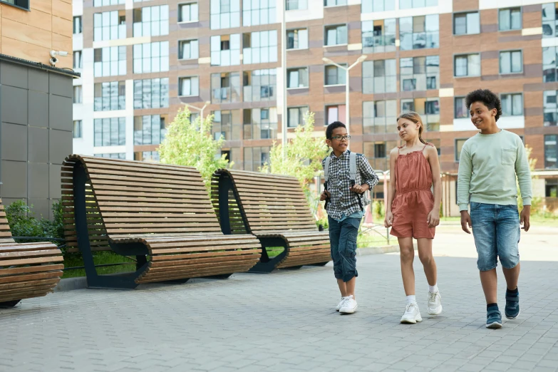 four children walk by wooden park benches on a sidewalk