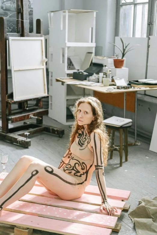 a young woman sitting on a wooden mat in an art studio