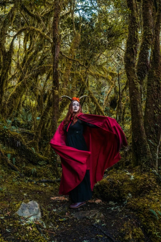 a young lady is walking in the woods with her long red cape