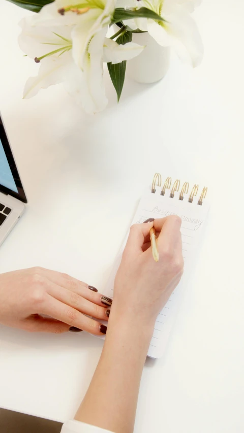 a women is writing on the white desk in her notebook