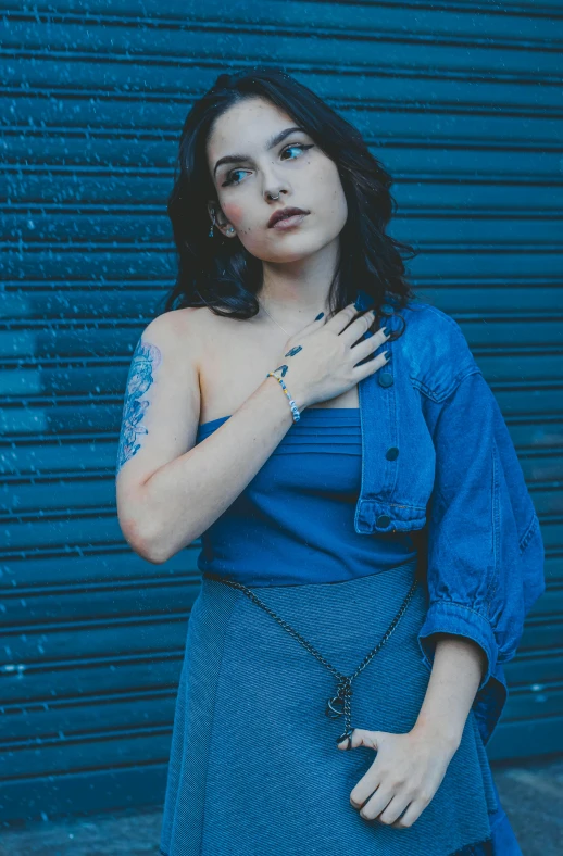 woman with dark hair wearing a blue dress standing next to a black building