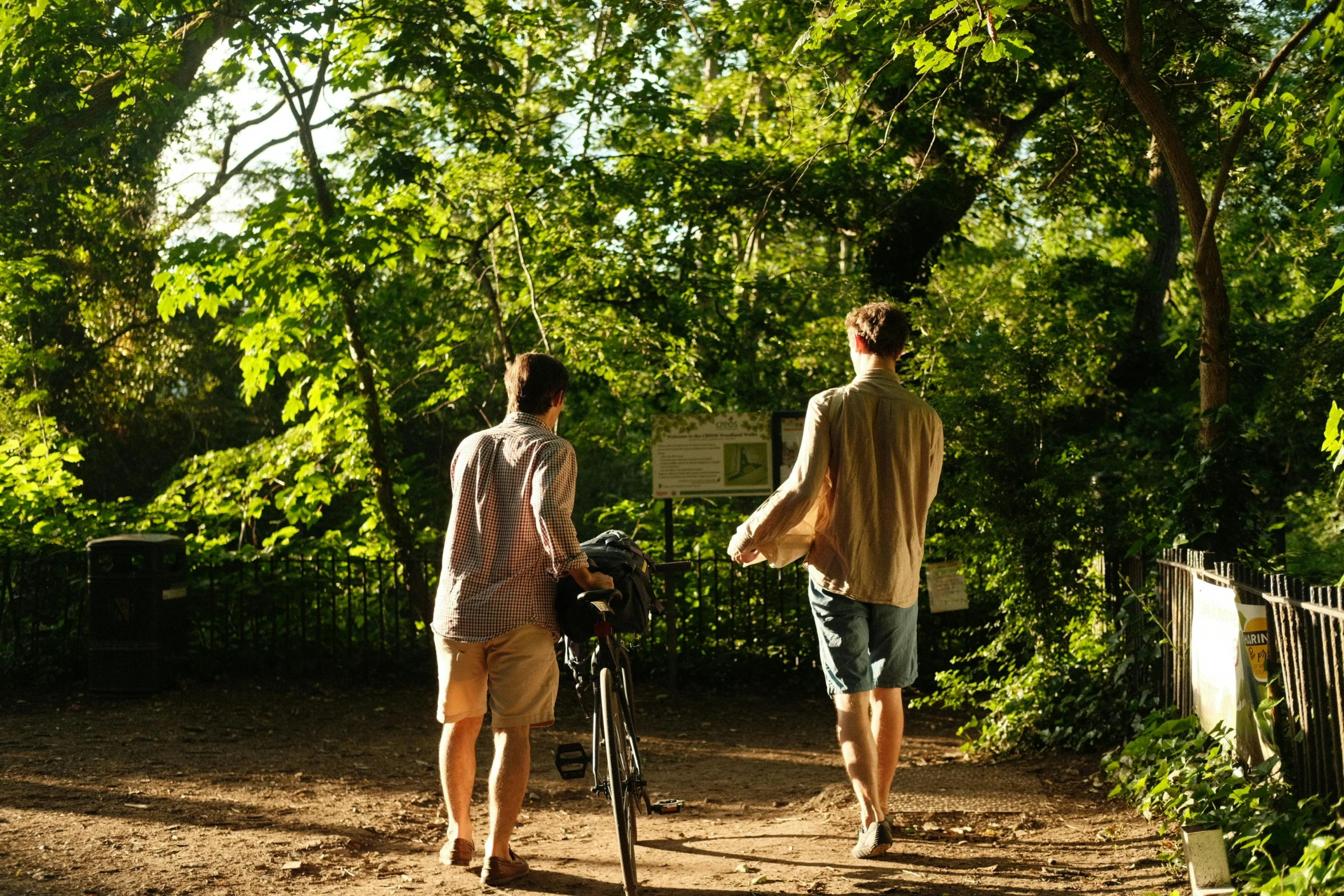 a couple of men walking their bikes down a dirt road