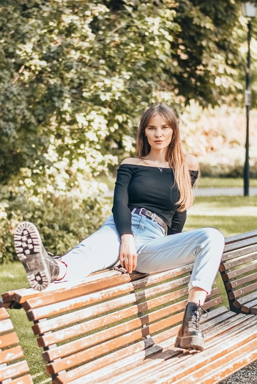 a woman sits on a bench near trees and grass