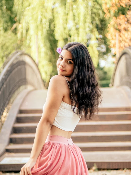 a woman in a skirt and crop top is standing by stairs