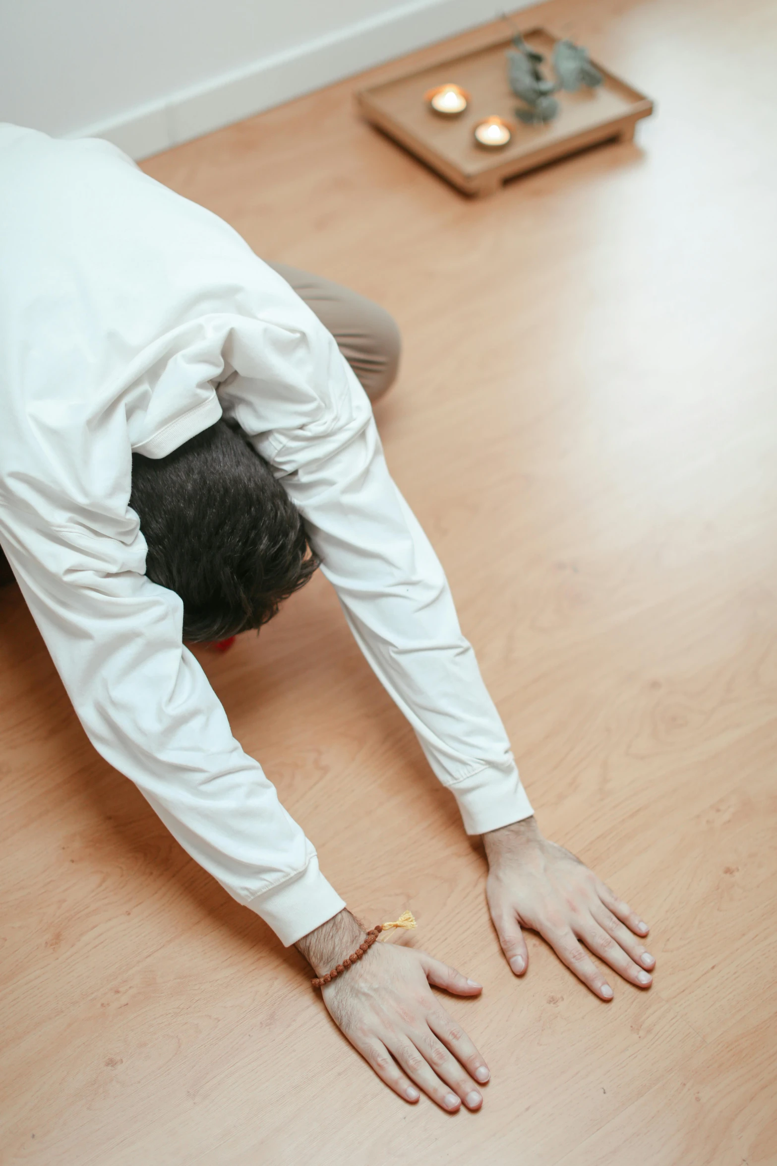 man dressed in white doing yoga on hard wood floor