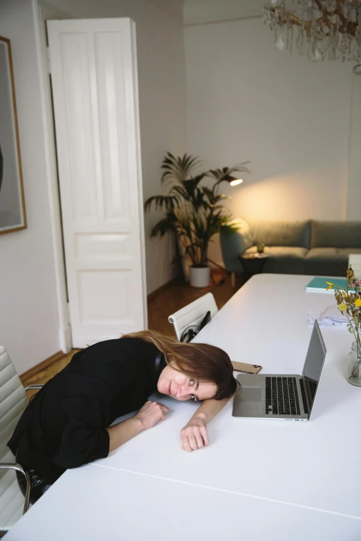 a woman in black shirt laying on table with laptop