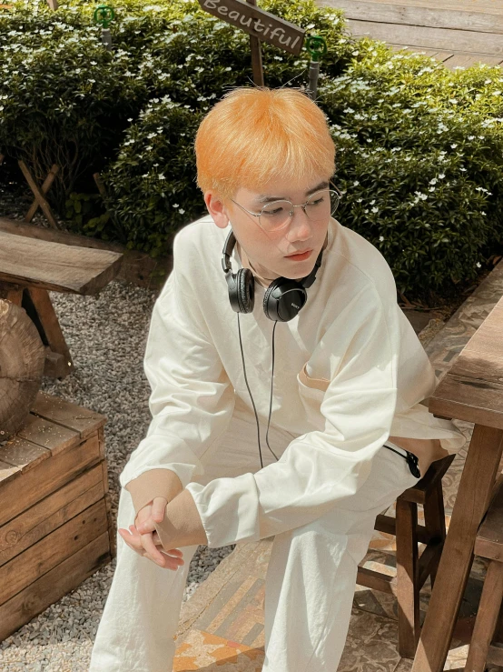 the man wearing white is sitting outside using headphones