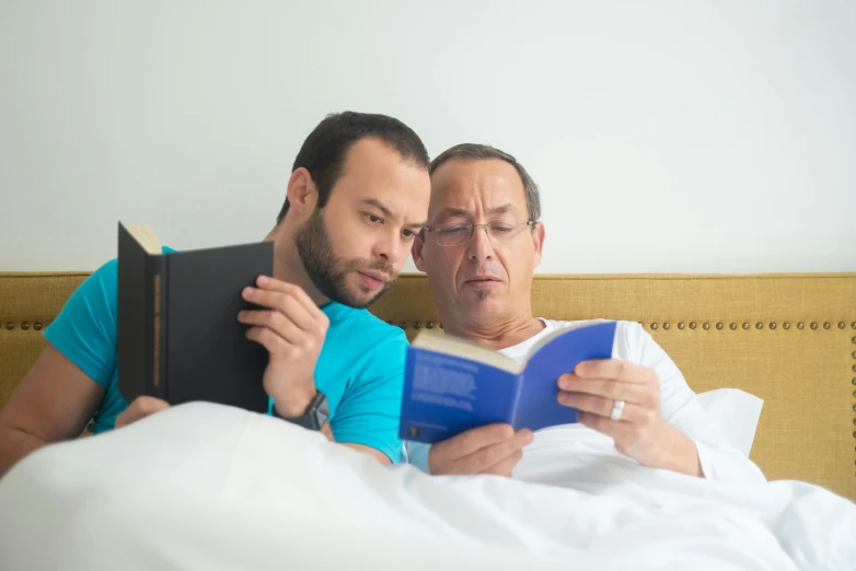 two people sitting on a bed reading a book