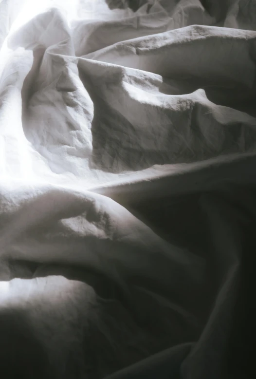 an unmade bed with white sheetding and sunlight streaming in