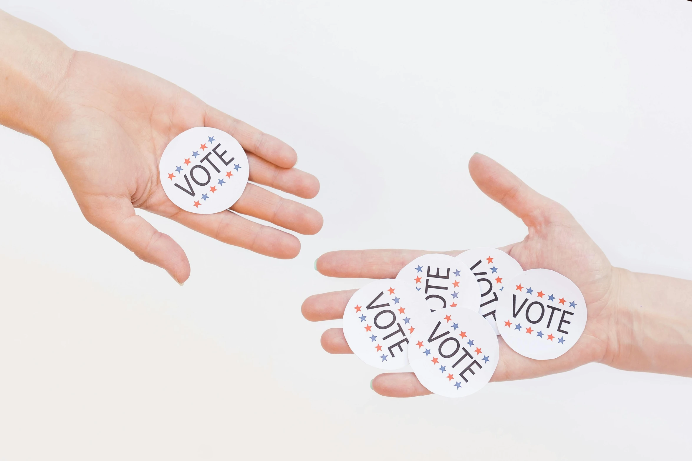 two people's hands holding three small stickers with a vote on it