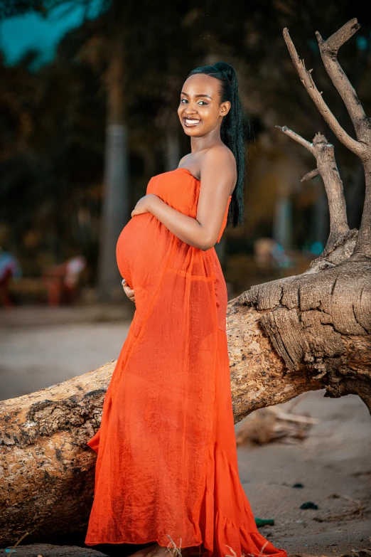 a woman in a bright orange dress smiles while standing near a tree